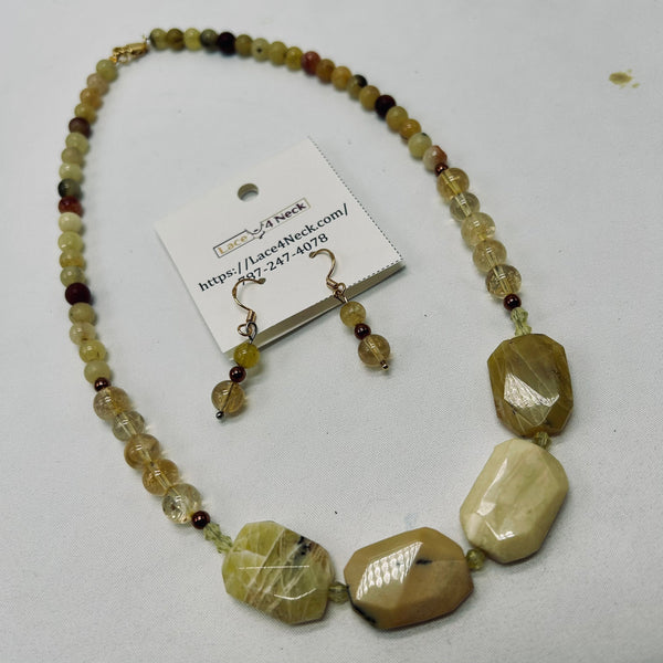 A beaded necklace and matching drop earrings displayed on a white background, with a small product tag attached. The jewelry features faceted natural stone beads in tan, cream, and olive tones, along with smaller translucent clear beads and a few dark reddish-brown accents.