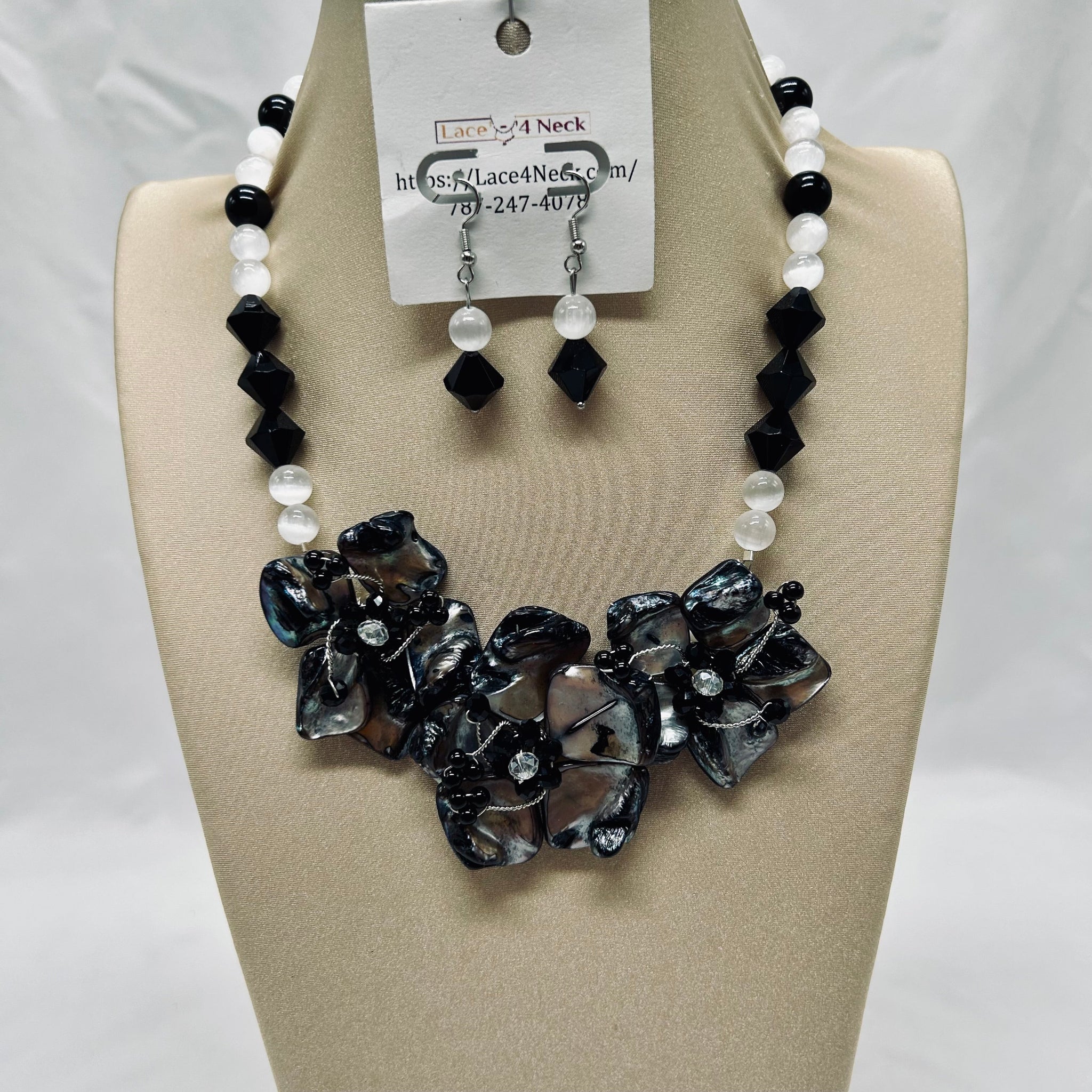 Necklace and earrings set on a beige display with a visible brand tag.