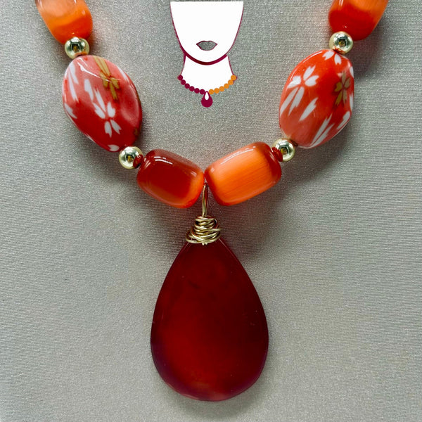 Necklace with red teardrop pendant and orange beads on a gray background