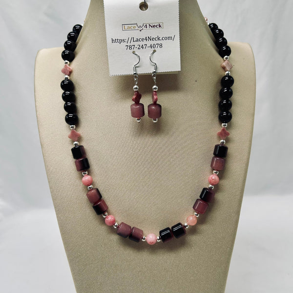 A beaded necklace and matching drop earrings displayed on a beige jewelry bust. The necklace features black beads, pink beads, and faceted maroon beads separated by small silver spacer beads.