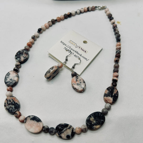 A beaded necklace and matching drop earrings made from polished and rounded stone beads with black, white, and pink marbled patterns, displayed on a white surface with a product tag attached.