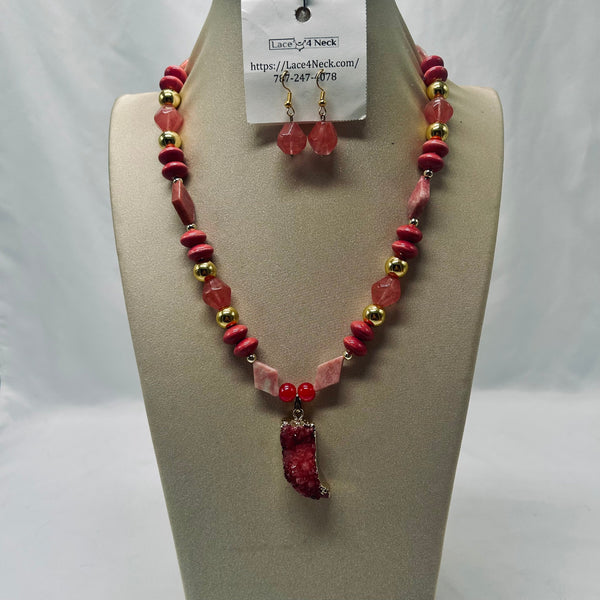 A beaded necklace and matching drop earrings displayed on a beige jewelry bust. The necklace features faceted pink and red beads with small gold spacer beads and a large polished red pendant.