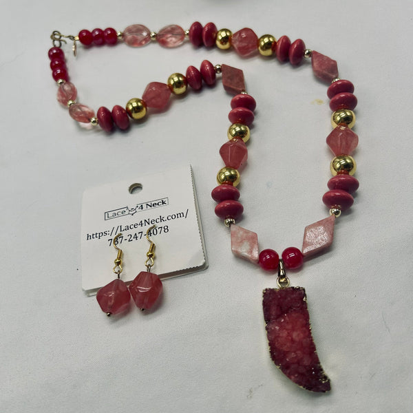 A beaded necklace and matching drop earrings displayed on a light gray background. The jewelry features pink and red beads, clear faceted beads, gold spacer beads, and a large pink geode pendant.